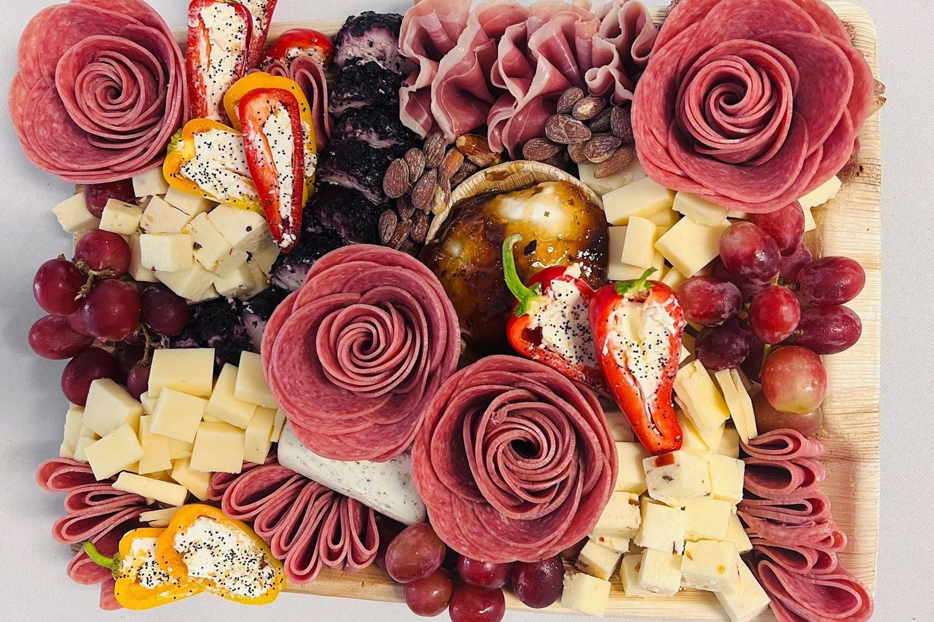 Elegant charcuterie board with rose-shaped cured meats, cheeses, and stuffed peppers.